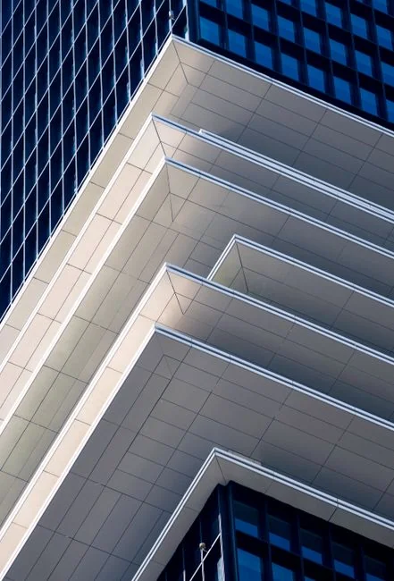 Trois laveurs de vitres suspendus à des cordes nettoient en journée la façade en verre d’un bâtiment moderne.