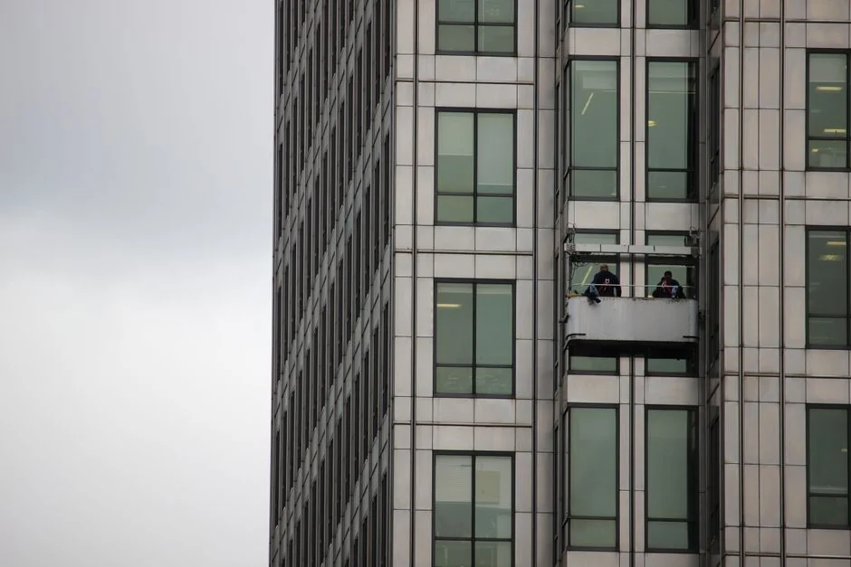 A worker cleaning skyscraper windows with a harness in an urban setting.